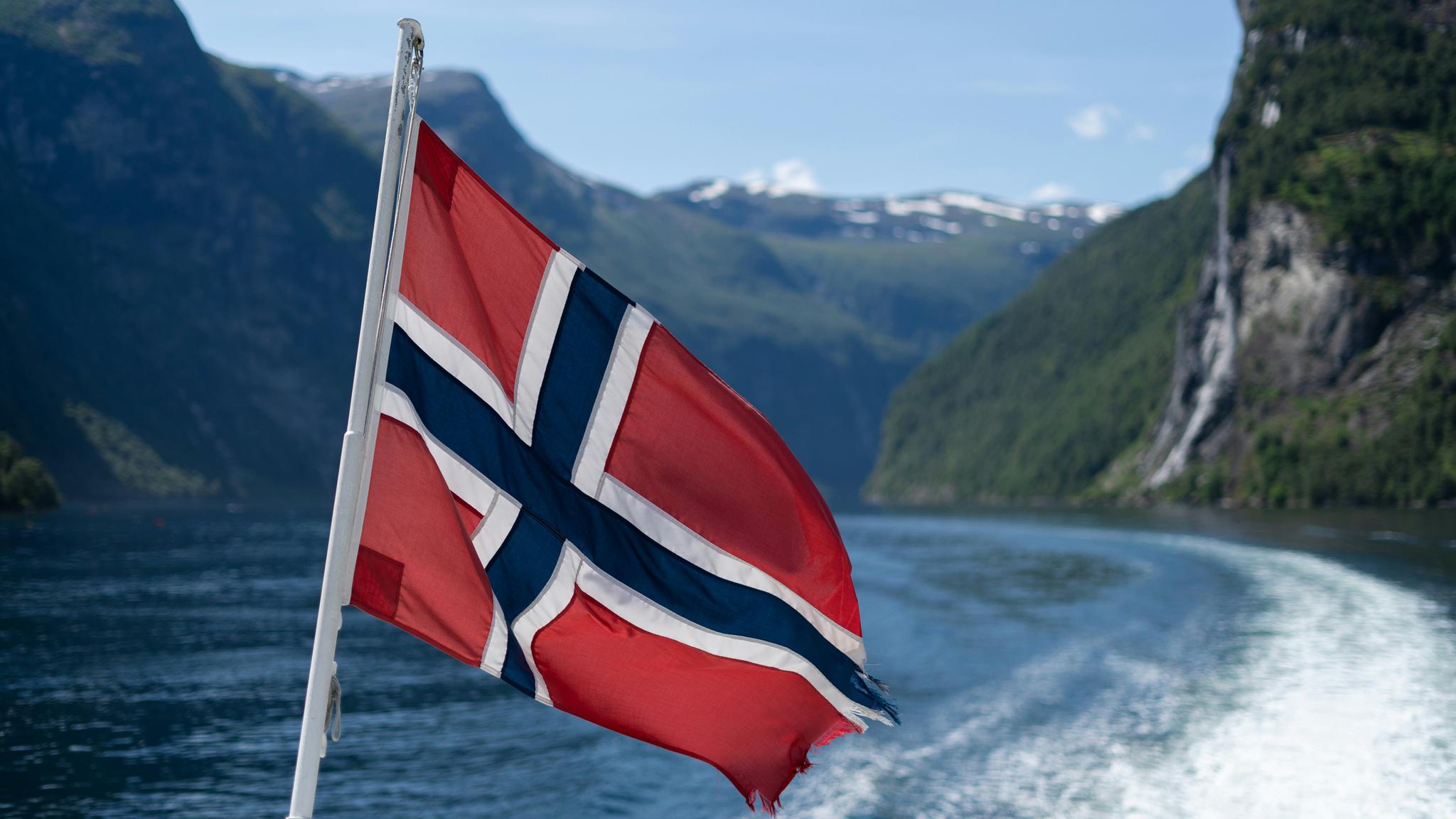 A Norwegian flag flying at the stern of a boat in a fjord