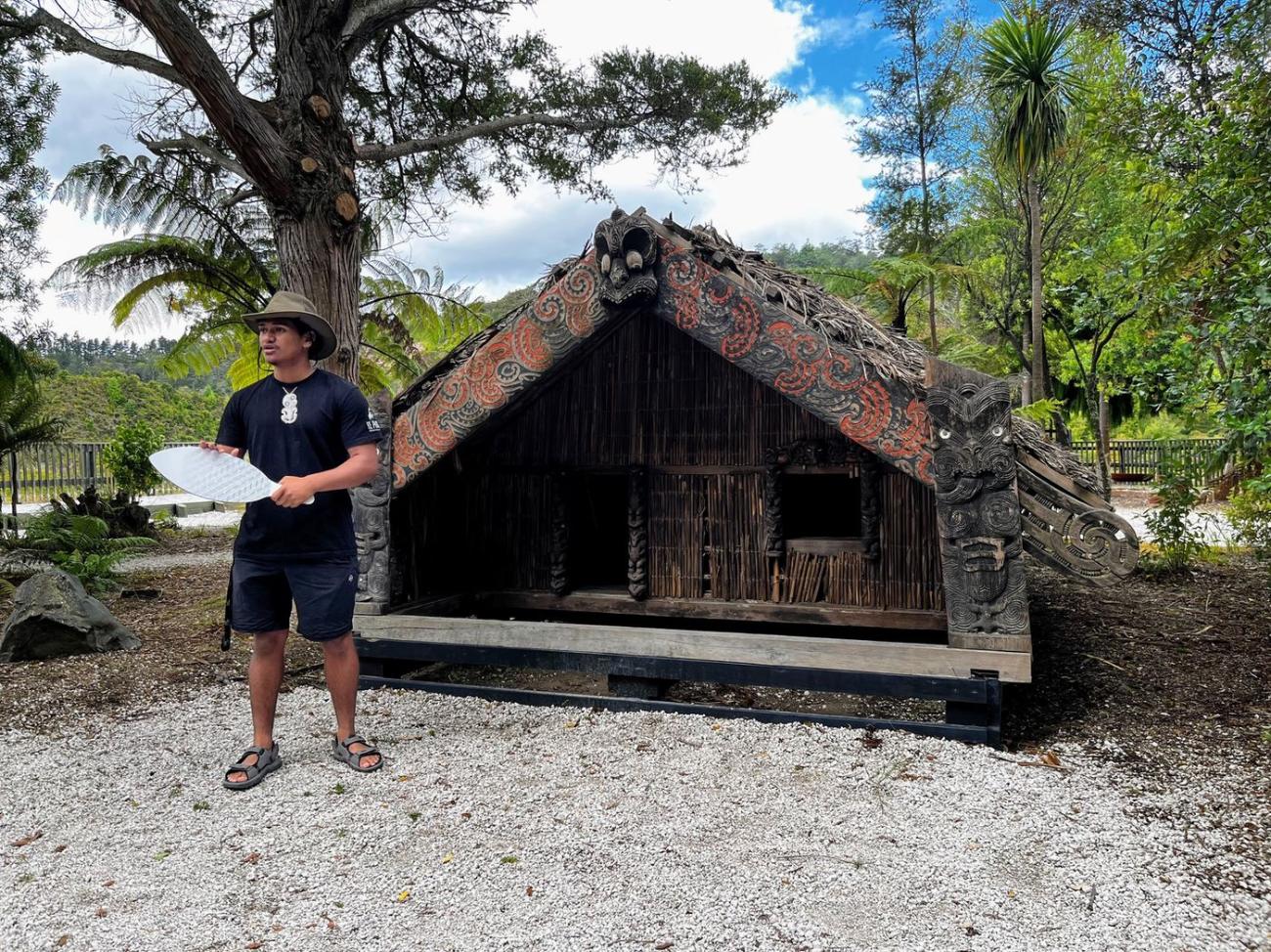 A Māori guide speaking in front of a carved meeting house in Rotorua