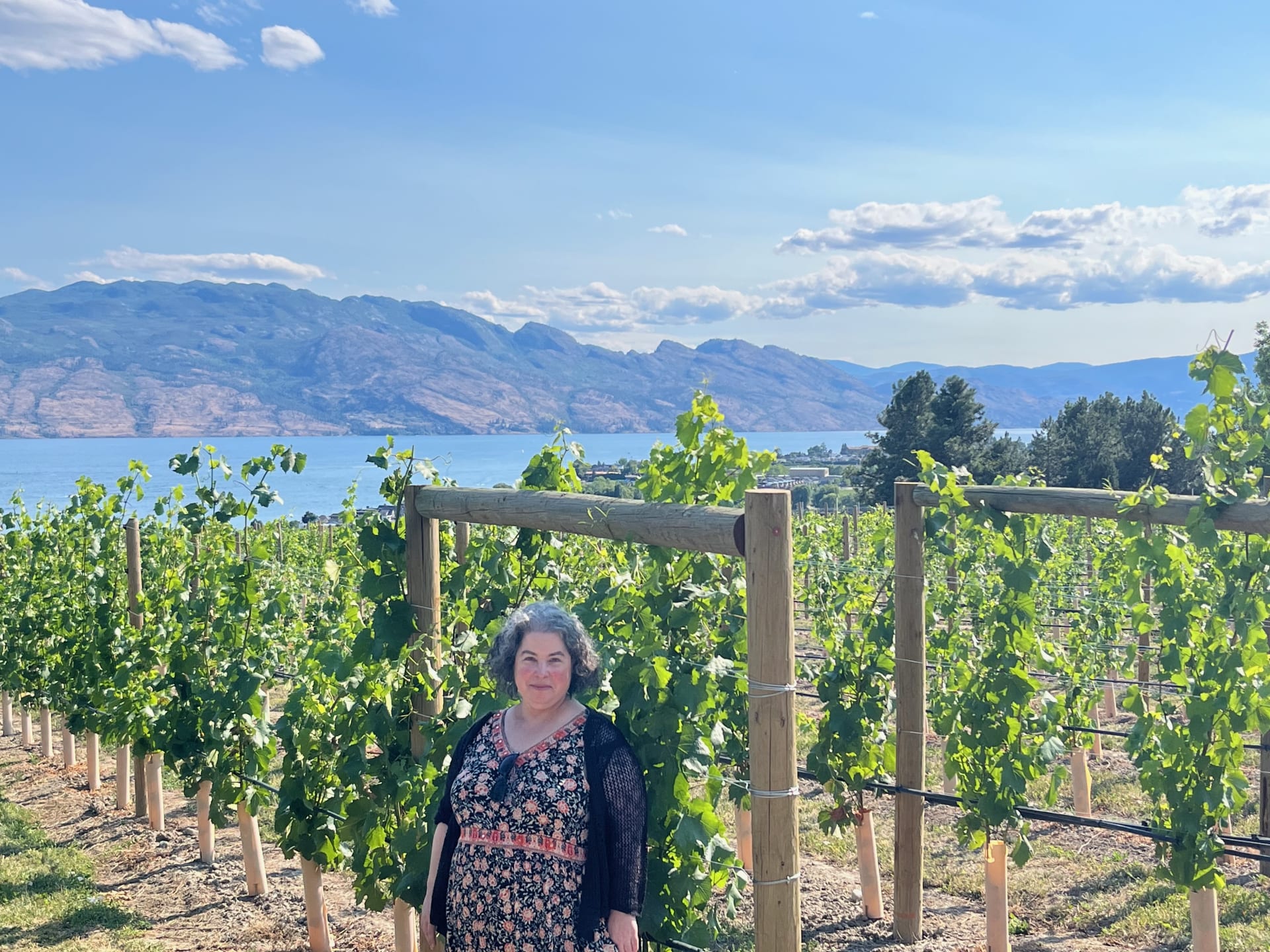 Rebecca Novick smiling in a sunlit vineyard above a lake